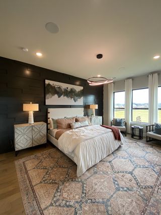 A spacious bedroom featuring a dark accent wall, cozy bedding, elegant lamps, and a beautiful patterned rug. 