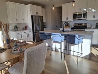 Model Home A modern kitchen with white cabinets, an island with blue stools, and a cozy dining area featuring elegant decor.