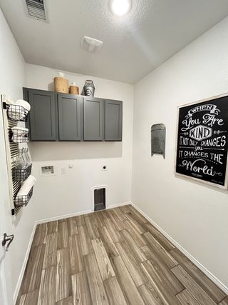 A functional laundry room featuring gray cabinets, wood-look tile flooring, and stylish decor accents.