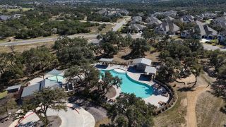 An elevated view of the Caliterra community by Drees Custom Homes in Dripping Springs, TX, highlighting the community pool and recreational areas nestled among mature trees.