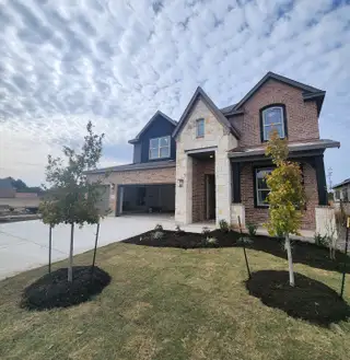 A beautiful brick home with a stone entryway and fresh landscaping in Hawkes Landing by Brightland Homes (Leander, TX).