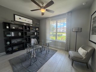 A modern office with sleek glass desk, stylish gray shelving, and large window, complemented by chic decor and a cozy chair.