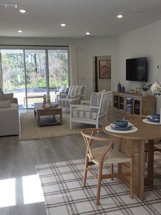 A bright living area with modern decor, featuring wide glass doors, striped chairs, and a cozy dining space.
