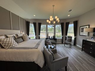 Model Home A spacious bedroom featuring elegant gray tones, a luxurious bed, modern chandeliers, and large windows with serene views.