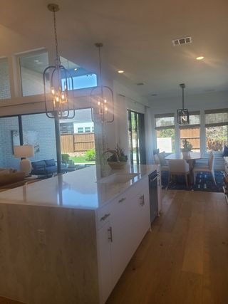 A bright open-plan kitchen and dining area with a large marble island, elegant lighting, and natural light pouring in.