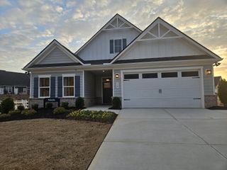 A charming gray home with shutters, a landscaped yard, and a welcoming porch in Newberry 55+ by Ryan Homes (Mcdonough, GA).