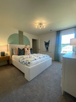 A cozy bedroom with plush carpeting, abstract artwork, and a stylish bed. Elegantly lit by a modern ceiling fixture.