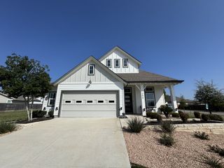 Street view A charming white home with a manicured yard in Trace by Chesmar Homes (San Marcos, TX).