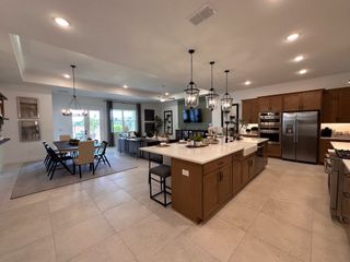 An elegant open-plan kitchen and dining area with modern lighting, wooden cabinetry, and sleek stainless steel appliances.