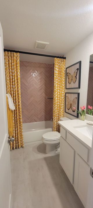 A bright bathroom with pink herringbone tile, white cabinets, and yellow curtains offers a cheerful, modern space.