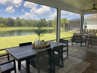 A serene patio with elegant outdoor furniture overlooking a tranquil pond and lush greenery under a bright blue sky.