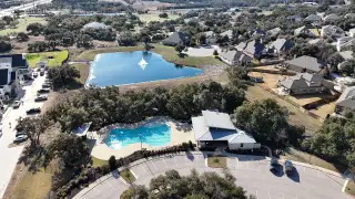 Community Amenities A serene aerial shot of the Palmera Ridge community by Highland Homes, featuring a tranquil pond and beautifully landscaped areas in Leander, TX.