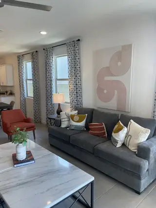 Model Home A modern living room with a sleek gray sofa, patterned curtains, and a marble coffee table, accented by stylish decor.