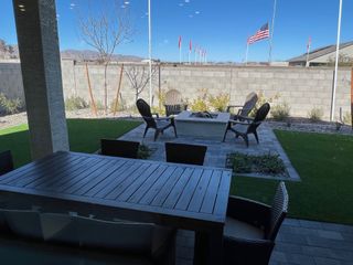 A cozy patio with a dining set, Adirondack chairs, and a fire pit, framed by a stone wall and lush greenery.