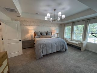 A cozy bedroom featuring a plush bed, elegant chandelier, and natural light from large windows with scenic views.