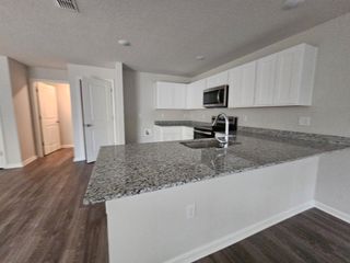 Model Home A sleek kitchen with granite countertops, white cabinetry, and wood flooring, offering a modern space for cooking and entertaining.