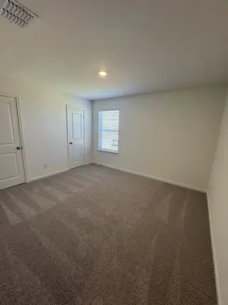 A spacious bedroom with soft carpeting, neutral walls, a window, and a double-door closet for ample storage.