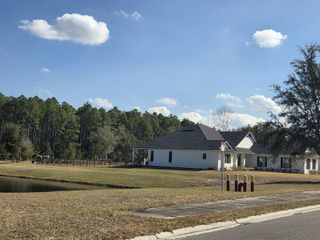 A charming white home by a pond with a backdrop of lush trees in Edwards Creek Estates by SEDA New Homes (Jacksonville, FL).