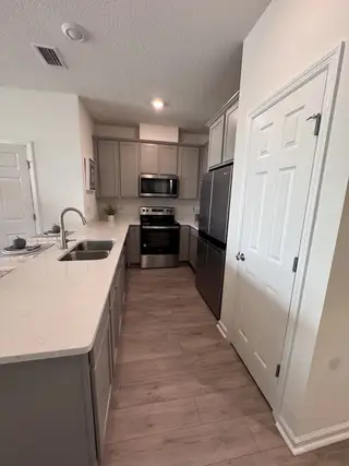 Model Home A modern kitchen featuring sleek grey cabinets, stainless steel appliances, and elegant wood flooring.