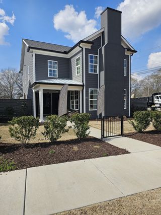A modern two-story home with dark gray siding, white trim, and a prominent chimney stands as a model home in Harmony by Kinglett Homes (Auburn, GA).