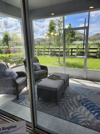 A cozy sunroom with wicker seating, a patterned rug, and lush greenery views through large windows.