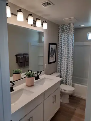 A modern bathroom with dual sinks, elegant lighting, white cabinetry, and geometric shower curtains.