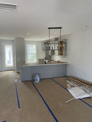 A modern kitchen under construction, featuring a sleek island, pendant lighting, and large windows.
