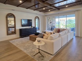 A cozy living room with wooden ceilings, a plush white sofa, and large windows overlooking a landscaped view.