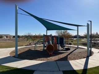 Community Amenities A vibrant playground with shade sails in The Palms Collection at The Trails at Tortosa by Century Communities (Maricopa, AZ).