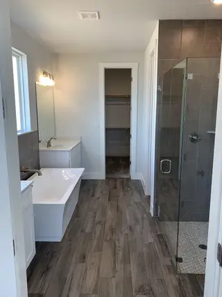 A modern bathroom with a sleek glass shower, freestanding tub, white vanity, and wood-look tile flooring.