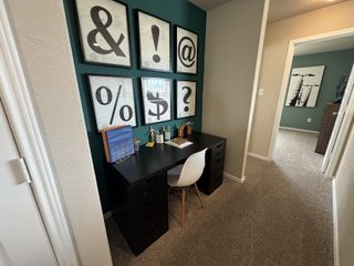 Compact workspace with a sleek black desk, modern wall art, and a white chair against a teal accent wall.