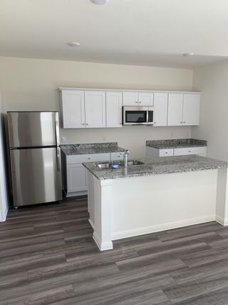 A modern kitchen with granite countertops, white cabinets, stainless steel appliances, and wood-like flooring.
