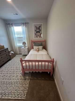 A cozy kid's bedroom with a pink bed frame, patterned rug, and butterfly artwork, creating a charming and inviting space.