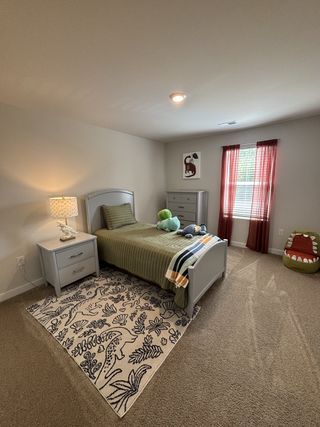 Model Home A cozy child's bedroom with an olive bedspread, dinosaur-themed rug, and bright decor accents.