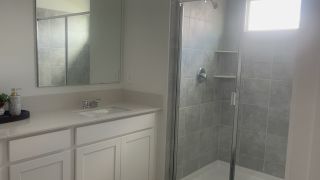 A sleek bathroom with a glass shower, light gray tiles, and a modern vanity with ample counter space.
