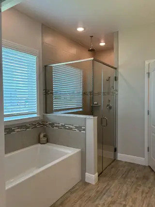 A modern bathroom featuring a sleek glass shower, spacious soaking tub, and warm wood-style flooring.