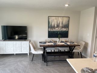 Model Home A modern dining area with a sleek table set, abstract art, and a large TV on a chic console.
