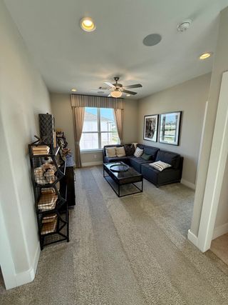 Model Home A cozy loft space with plush carpeting, a dark sectional sofa, and natural light. Ideal for a media room or casual living area.