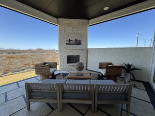 Model Home A cozy outdoor patio with modern seating, a stone wall, and a fireplace, perfect for relaxation and entertaining.
