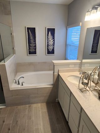 A cozy bathroom with a soaking tub, dual sinks, and elegant fern artwork. Natural light streams through the window.