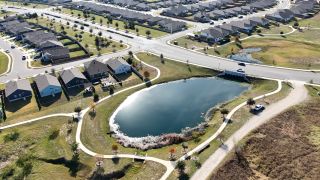 Community Amenities Charming aerial view of The Colony-Pine Cove by Sitterle Homes, featuring serene pond and landscaped pathways (Bastrop, TX).