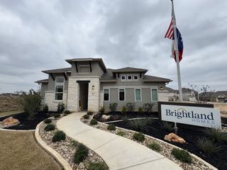 A stunning modern home with stone accents, a curved pathway, and lush landscaping in Veramendi by Brightland Homes (New Braunfels, TX).