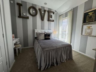 Model Home A cozy bedroom with striped walls, bold "LOVE" art, and light curtains, featuring a plush bed and chic decor.