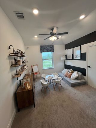 A cozy playroom with a carpeted floor, play table, wall art, and ample lighting perfect for creativity and fun.