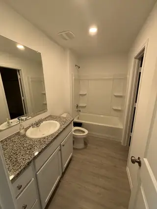 Model Home A clean, well-lit bathroom with a granite countertop, white cabinets, and a tub/shower combo.