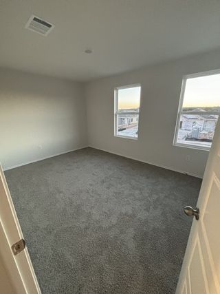 A bright room with plush gray carpet, white walls, and two large windows for ample natural light and serene views.