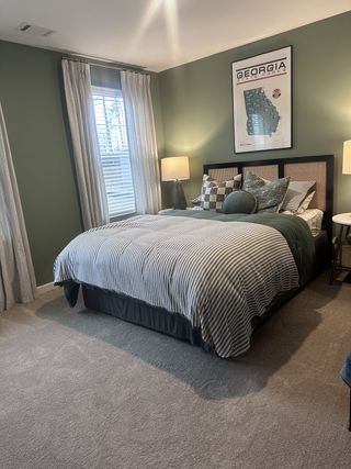 A cozy bedroom with green walls, patterned bedding, and elegant lighting, featuring a Georgia state parks poster.