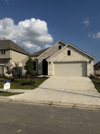 Street view A beautiful stone-front home with a clean driveway in Carillon by Brightland Homes (Manor, TX).