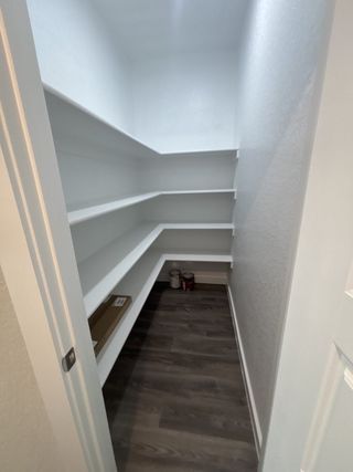 A spacious pantry with built-in white shelving and wood-like flooring in Vista Ridge by HistoryMaker Homes (Live Oak, TX).