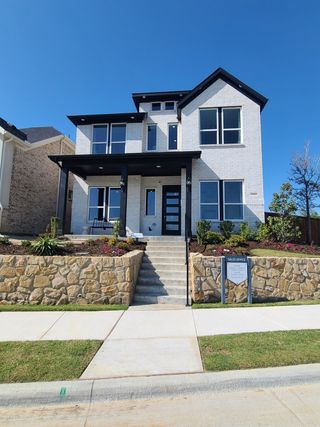 Street view A modern white brick home with black trim in Dominion at Brookhollow by Landon Homes, featuring a stone-bordered walkway (Prosper, TX).